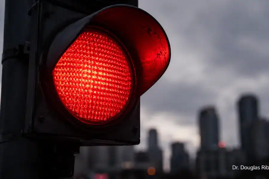 Semáforo vermelho aceso contra o céu nublado, simbolizando um sinal de alerta para sintomas de tontura que merecem atenção médica.